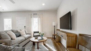 A modern living room with a sofa, armchairs, a coffee table, and a TV mounted on the wall. - Auburn Elite Retreat (Opelika)