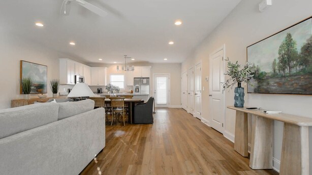 A spacious living area with a sofa, dining table, and chairs, a kitchen with cabinets and appliances, and a hallway with doors. - Auburn Elite Retreat (Opelika)