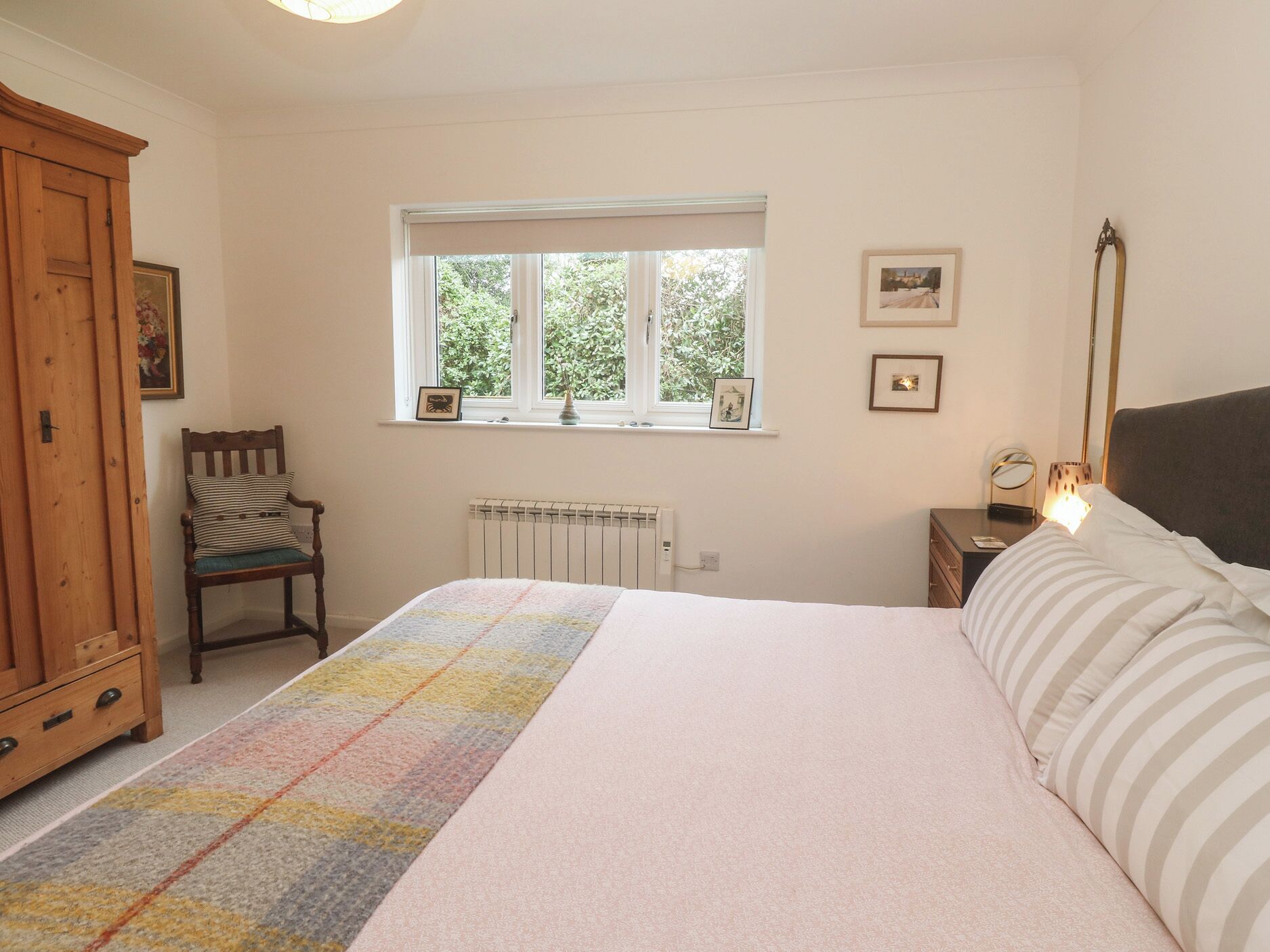 A bedroom with a bed, a chair, a nightstand, a radiator, and a window with pictures on the wall.