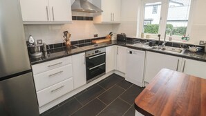 A modern kitchen with white cabinets, black countertops, and a wooden dining table. - Pump Cottage (Truro)
