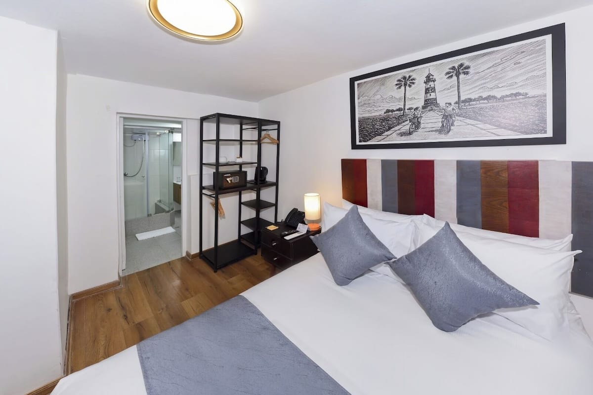 Una habitación de hotel con cama, mesita de noche, estantería y un cuadro en la pared.