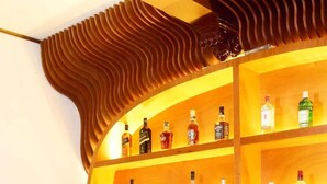 En bar med hylder fyldt med spiritusflasker, en bartender der laver en drink, og barudstyr på disken.