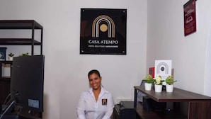 En receptionsdisk med logo for 'CASA ATEMPO HOTEL BOUTIQUE MIRAFLORES', en computerskærm, en plante og et indramet certifikat på væggen.
