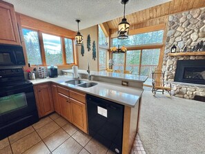 A kitchen with wooden cabinets, a dishwasher, a stove, a sink, and a stone fireplace.