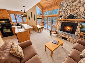 A cozy living room with a fireplace, a dining area, and a kitchen with a stone accent wall.