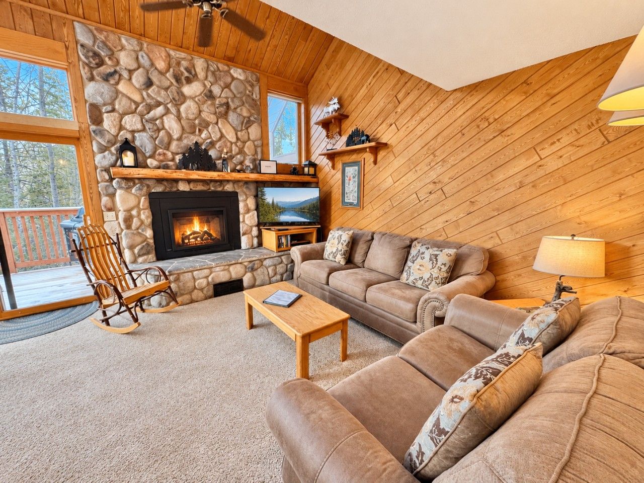 A cozy living room with a stone fireplace, wooden furniture, and a view of the outdoors.