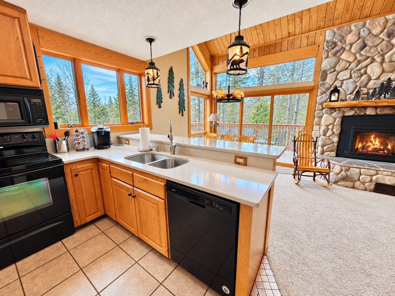 A modern kitchen with wooden cabinets, a dishwasher, a stove, and a stone fireplace.