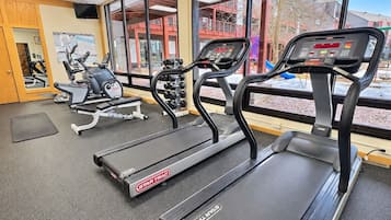 Een sportschool met loopbanden, een spiegelwand en een raam met uitzicht op gebouwen.