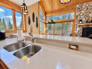 A kitchen with a double sink, wooden ceiling, stone wall, and large windows.