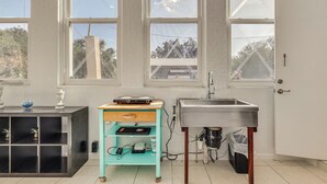 Una cocina con un lavamanos, una encimera con una balanza, un armario color turquesa y una ventana con vistas a árboles y un edificio.