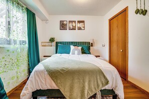 Un dormitorio con una cama, piso de madera, cortina verde y puerta de madera.