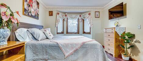 Un dormitorio con cama, cómoda y una ventana grande con cortinas.