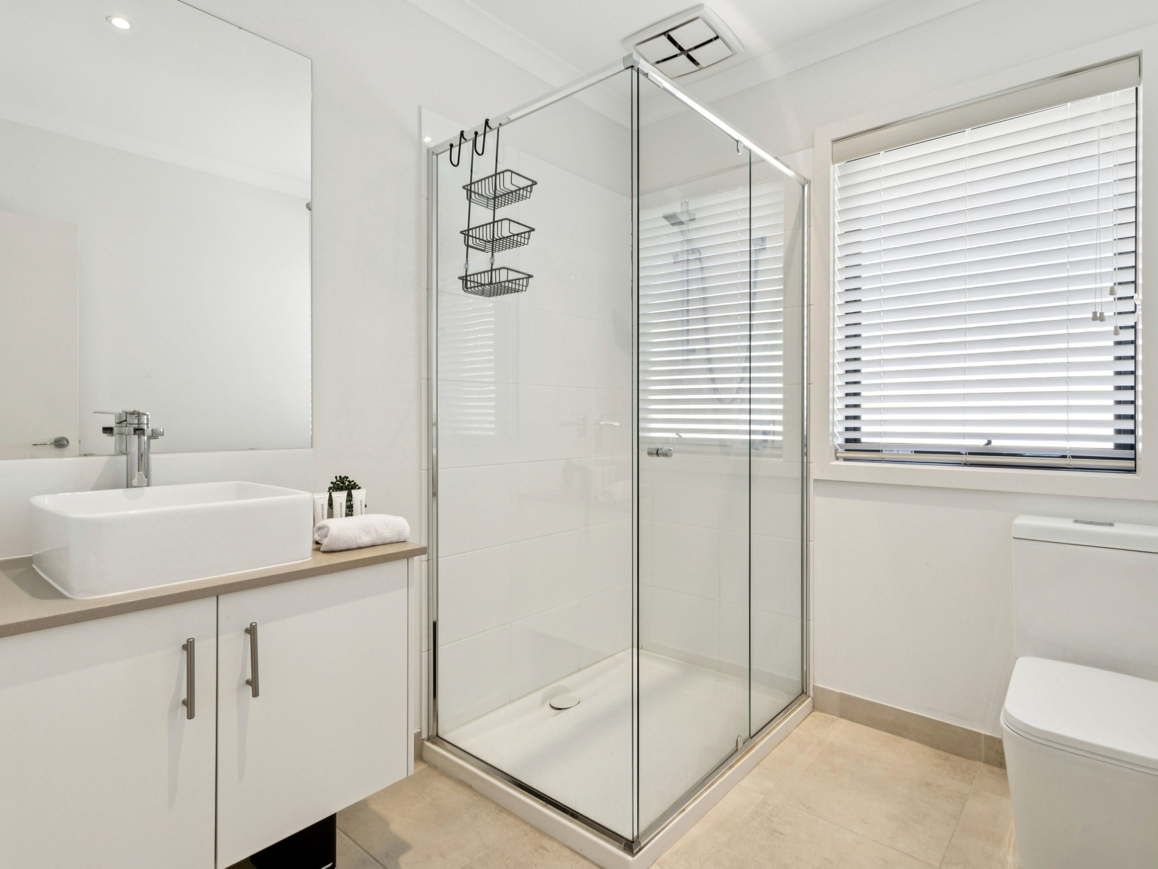 Et moderne badeværelse med et glasvægshus, et hvidt håndvask og et toilet.