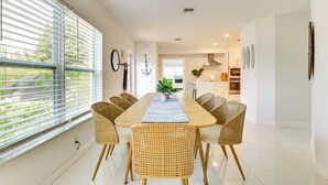 A modern dining area with a long table, wicker chairs, and a view through large windows. - 3 Mi to Sea! Family Pool House in Fort Lauderdale (Fort Lauderdale)