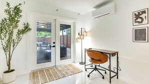 A modern room with a glass door leading to an outdoor area, a wooden desk, a potted plant, and a floor lamp. - 3 Mi to Sea! Family Pool House in Fort Lauderdale (Fort Lauderdale)