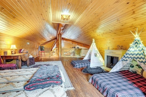 Interior acogedor de una cabaña de troncos con un dormitorio en el altillo, una chimenea y un tipi.