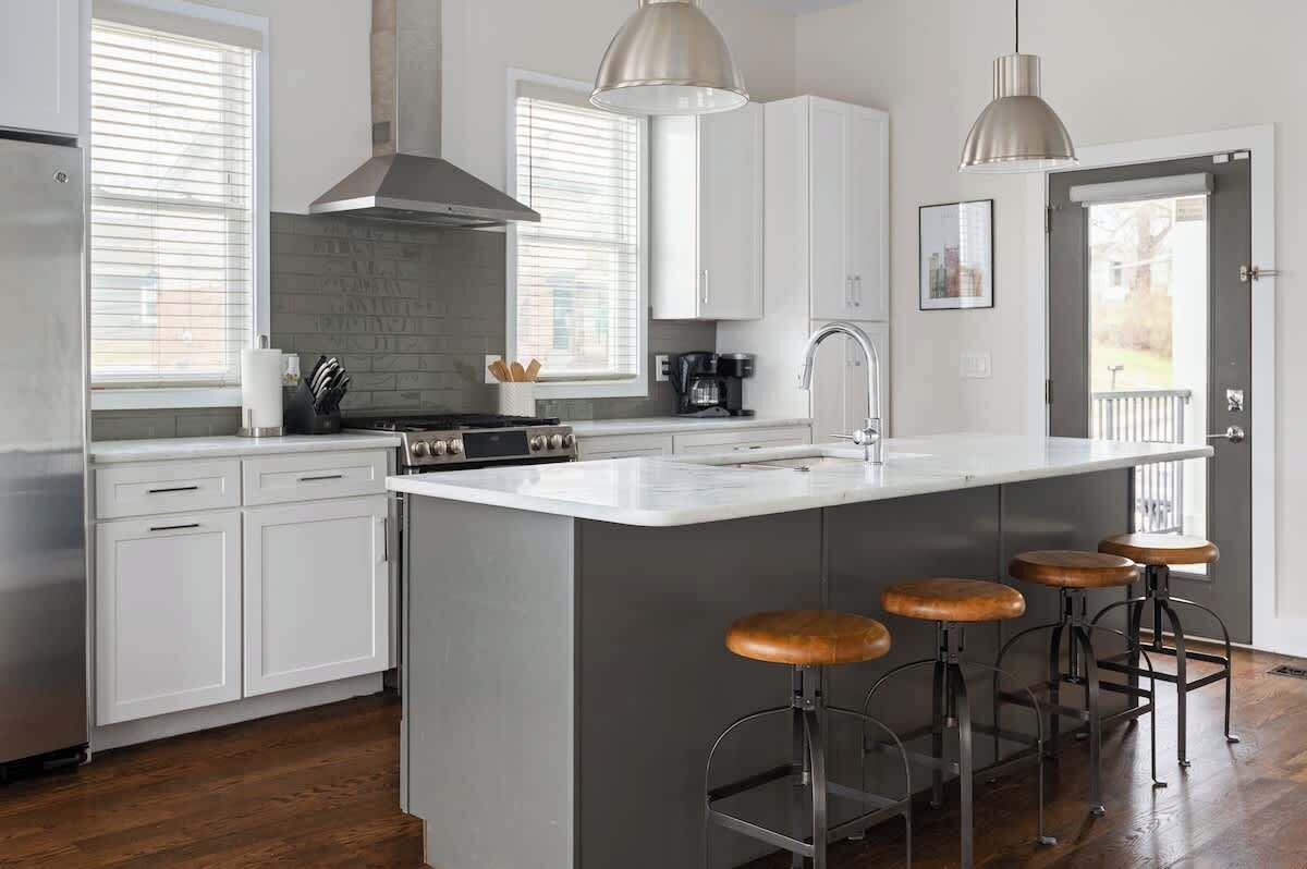 A modern kitchen with white cabinetry, a large island with stools, stainless steel appliances, and pendant lighting.