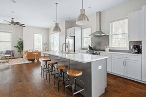 Una cocina moderna con una isla central, taburetes de bar, electrodomésticos de acero inoxidable y ventanas amplias.
