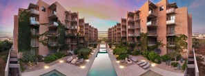 A modern hotel with a central pool, multiple balconies, and lush landscaping. - Las Arenas 1BR | Pool, Jacuzzi, Near Beach (Cabo San Lucas)