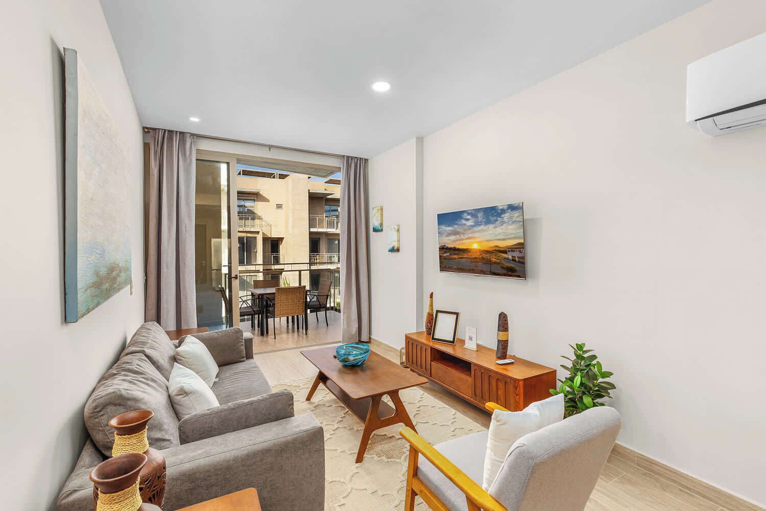 A modern living room with a sofa, coffee table, and TV. There is a balcony with a view of the city.