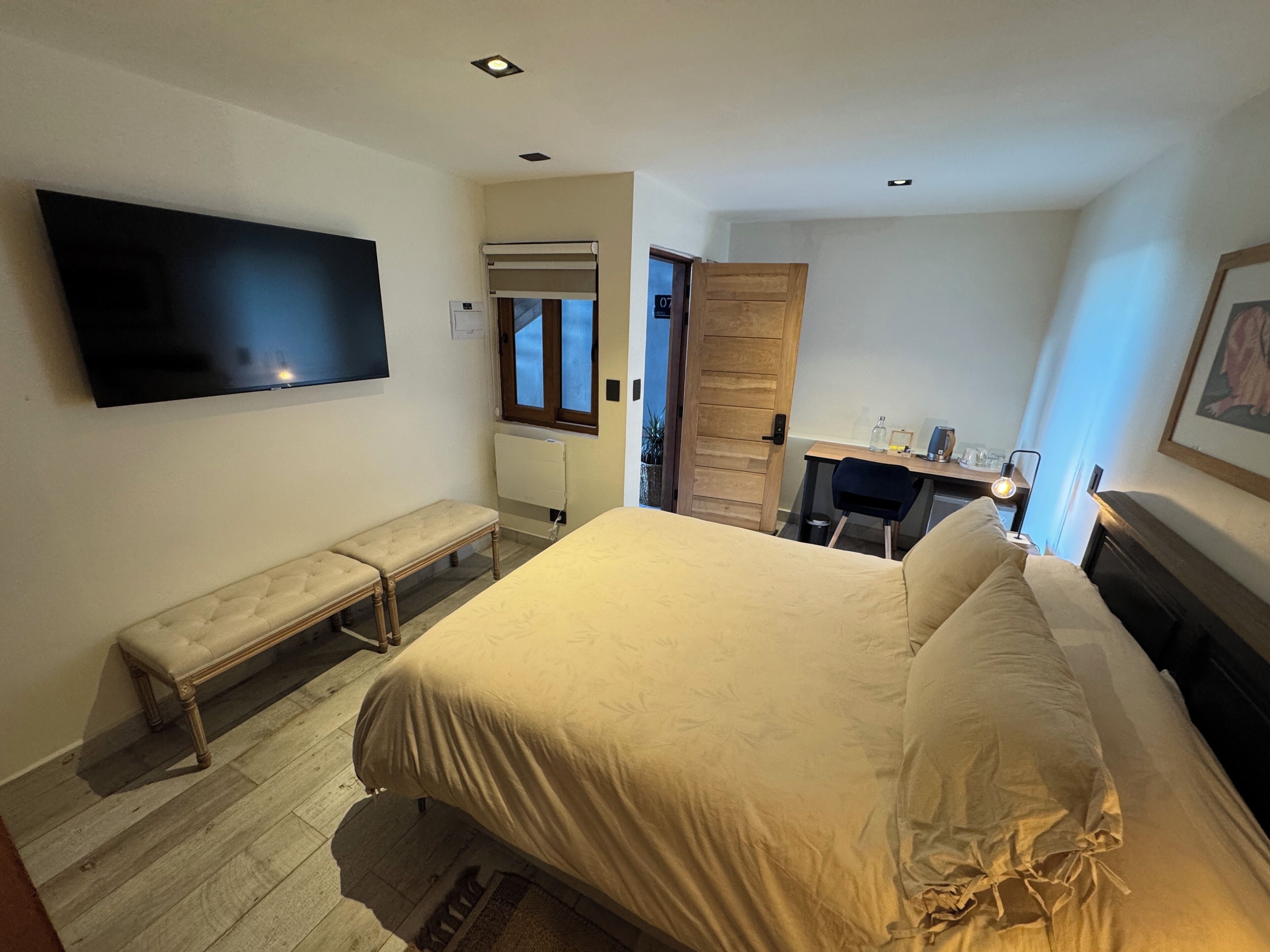 Een slaapkamer met een bed, een bankje, een bureau en een televisie.