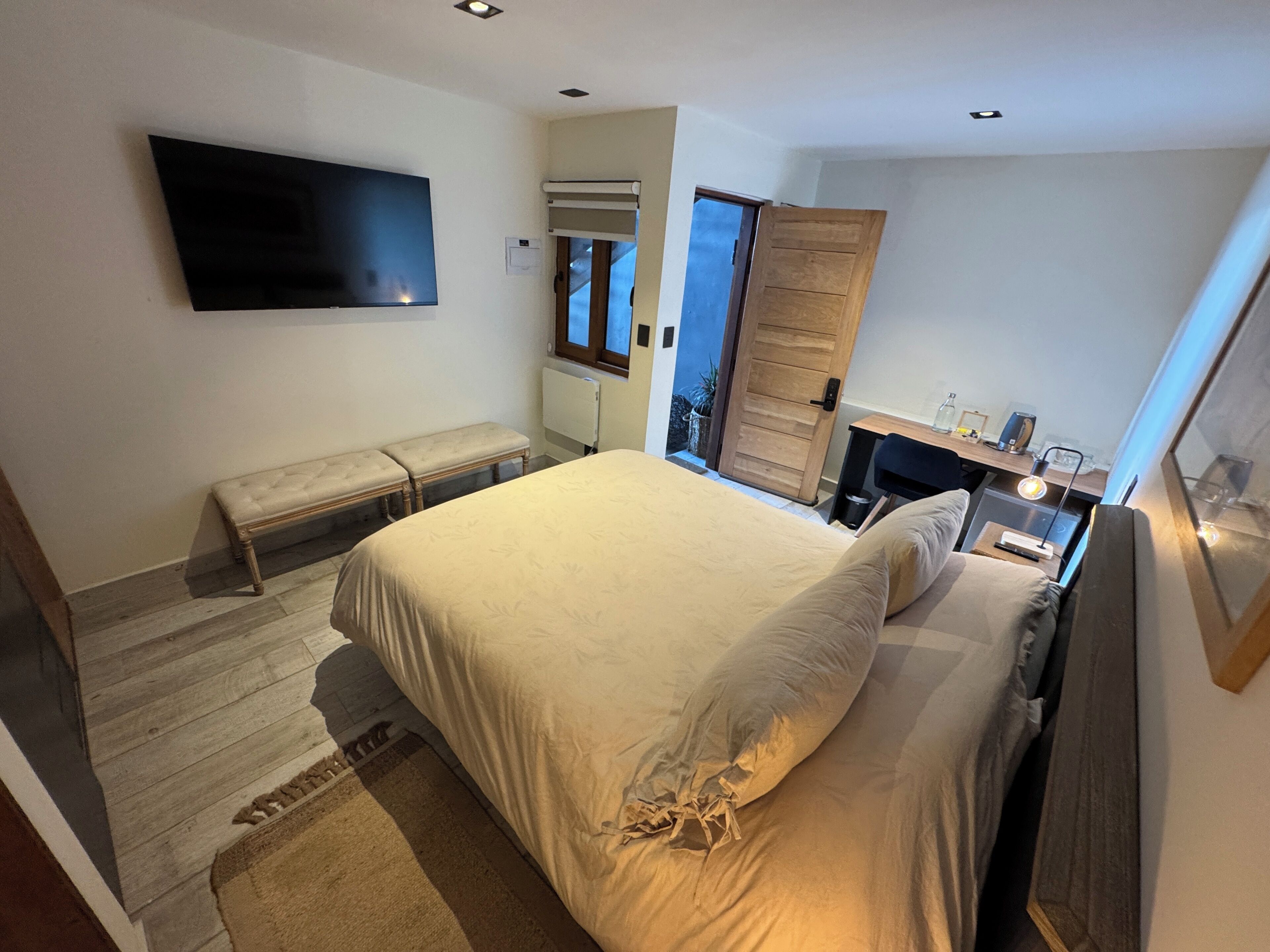 A bedroom with a bed, bench, bedside table, and a TV mounted on the wall.