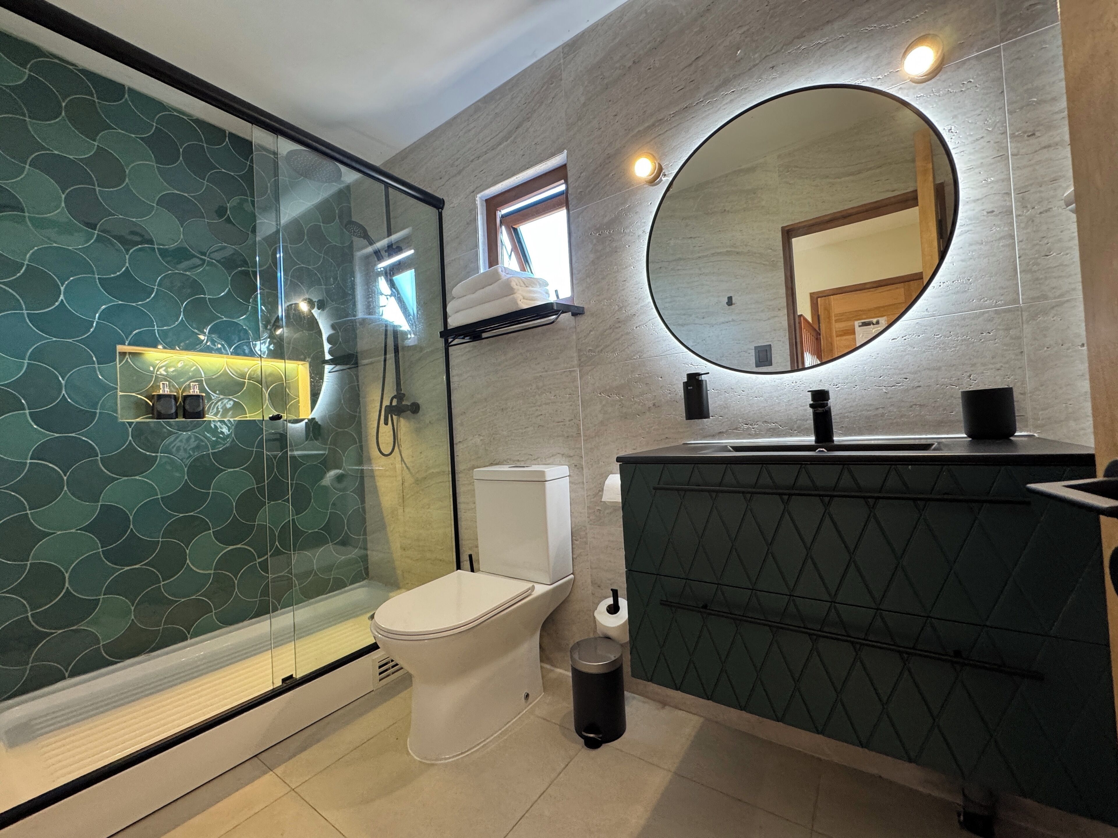 Et moderne badeværelse med et glasafskærmet brusebad, toilet, håndvask med spejl og en bøjle til håndklæder.
