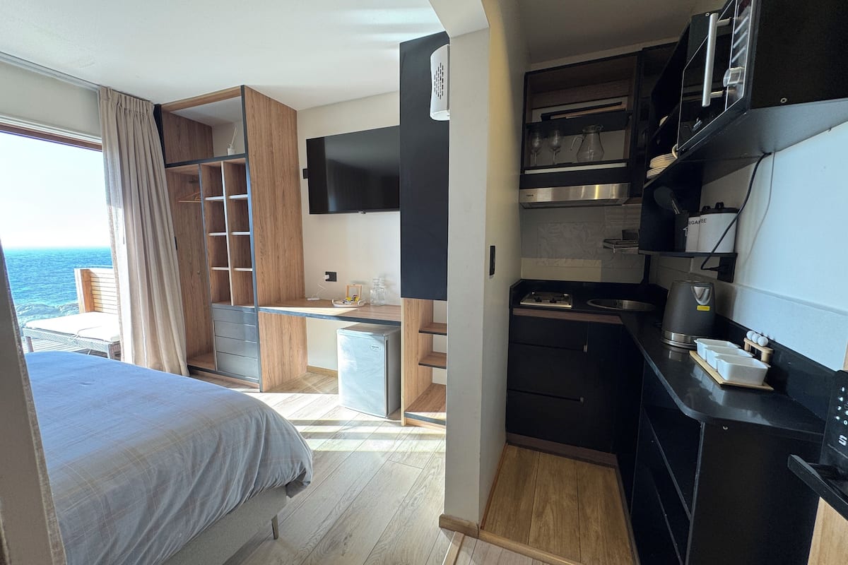Una habitación compacta y moderna con cama, kitchenette y vista al mar.
