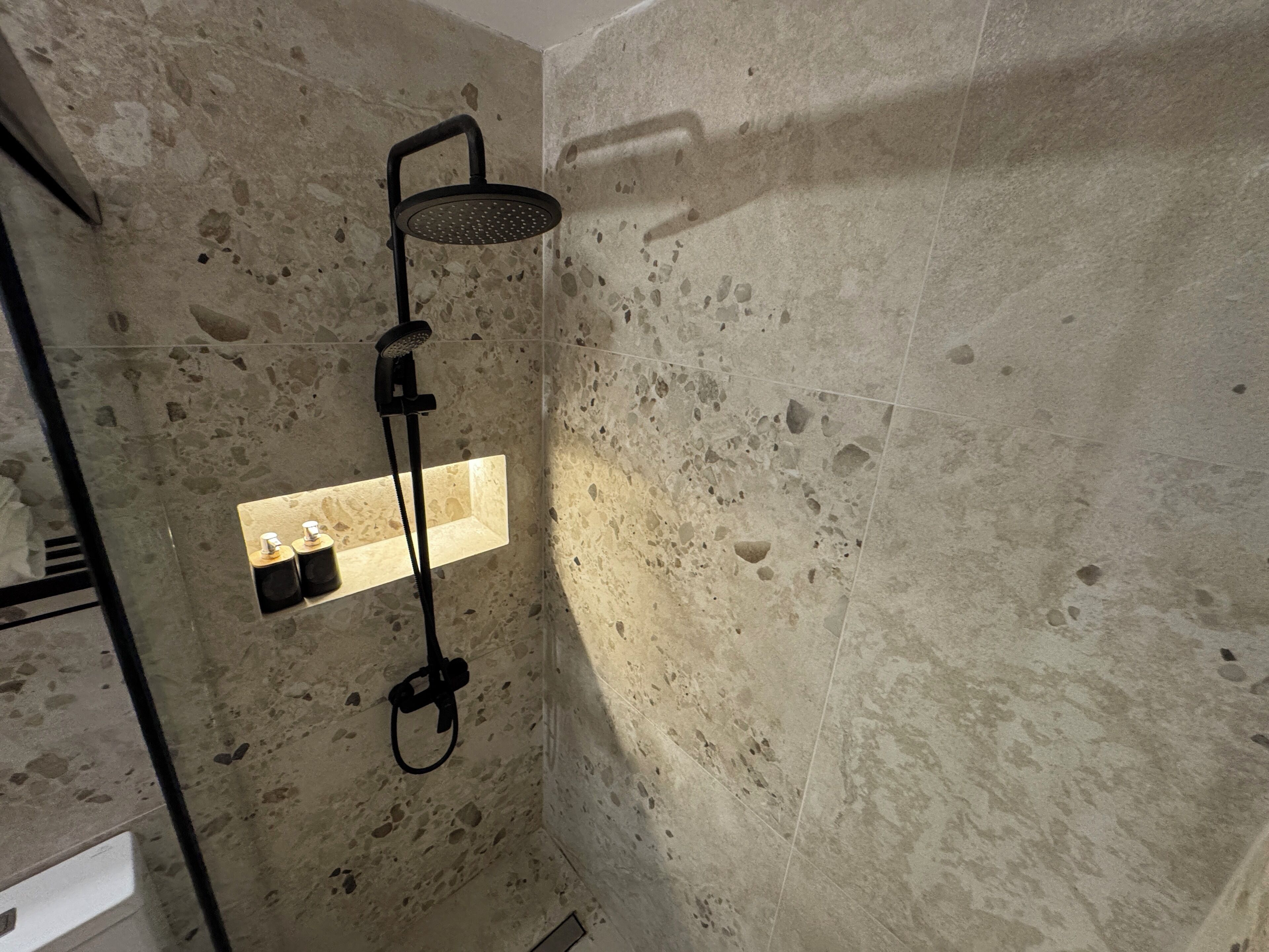 Ducha con cabezal de ducha de mano y panel de control en la pared.