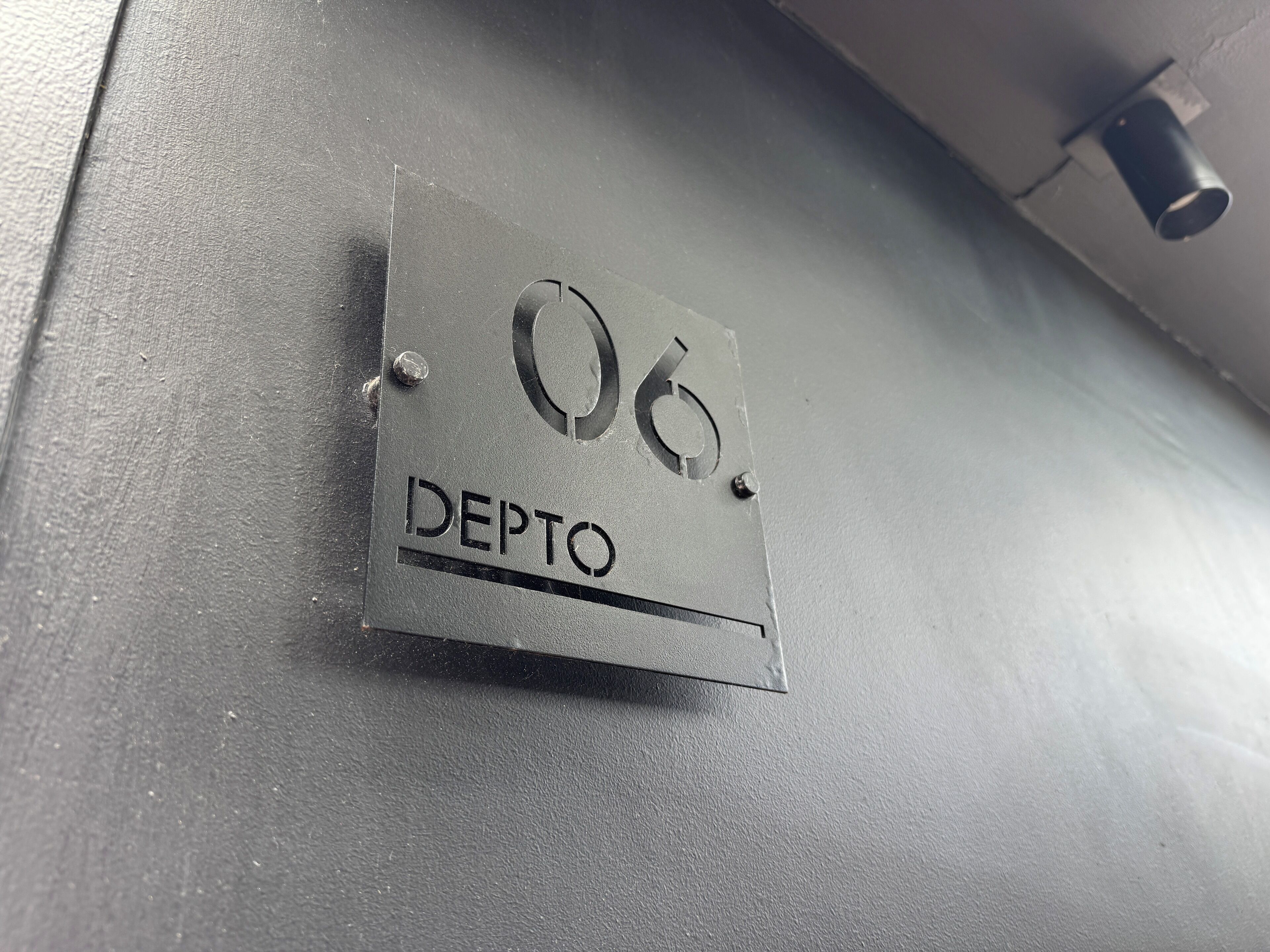 Un letrero metálico con el número 06 y la palabra 'DEPTO' en una pared.