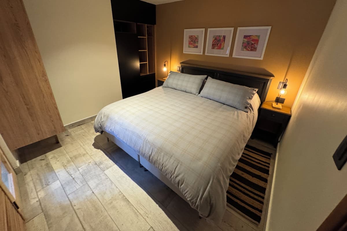 Un dormitorio con una cama grande, suelo de madera, un armario empotrado y tres cuadros enmarcados en la pared.