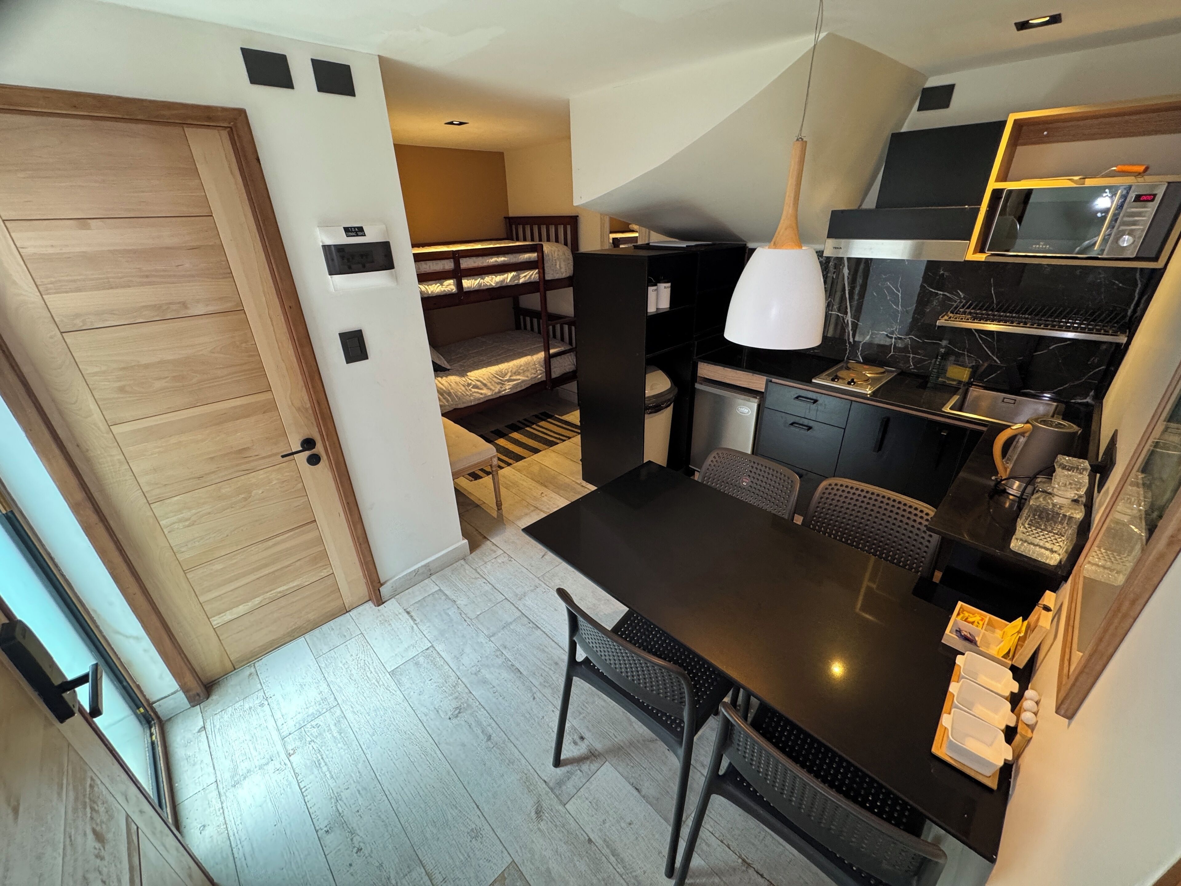 A compact kitchen with a microwave, stove, and sink. There is a small dining area with a table and chairs. A bunk bed is visible in the background.