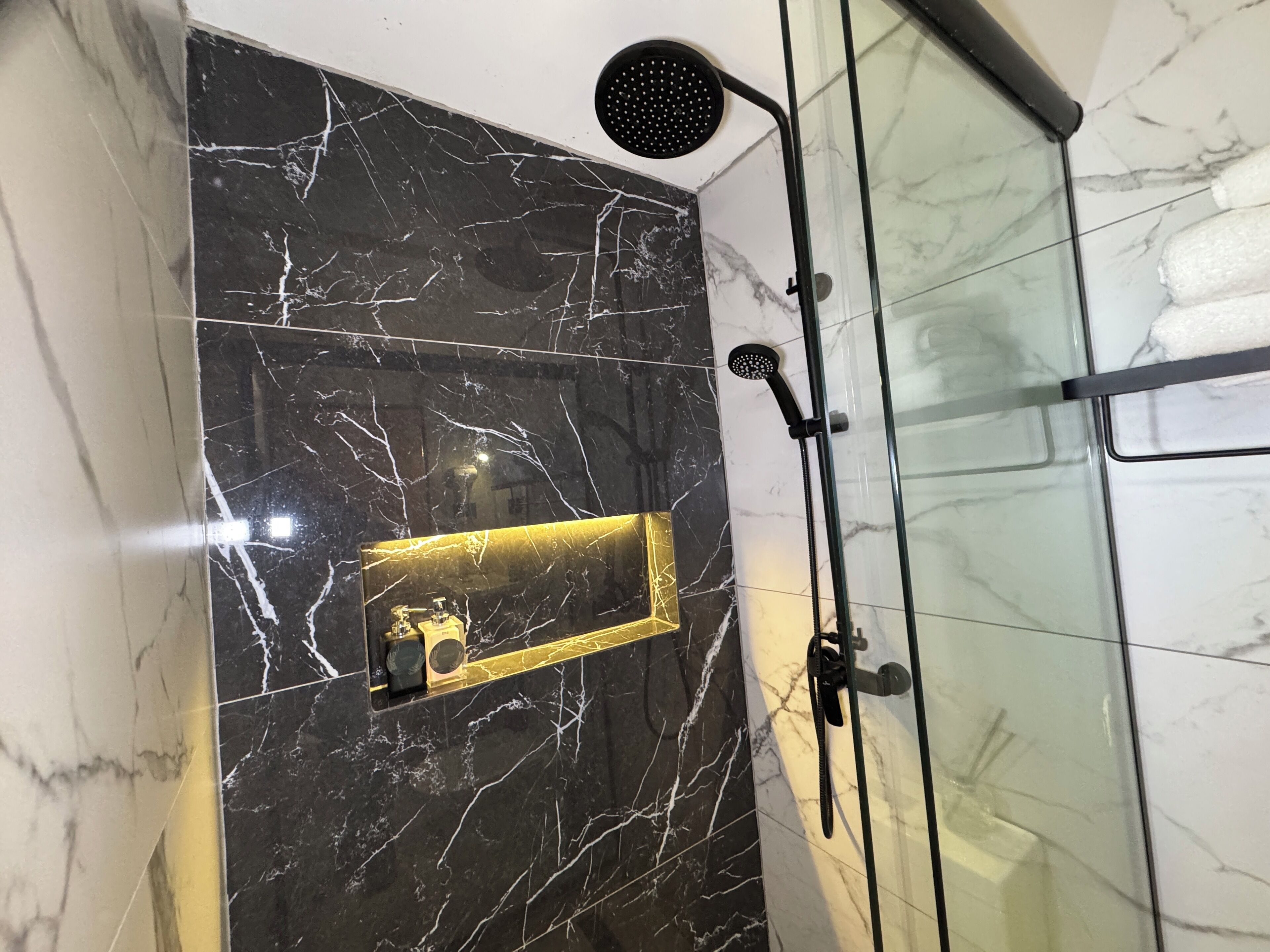 A bathroom with a glass shower enclosure, a gold-framed mirror, and a marble backsplash.