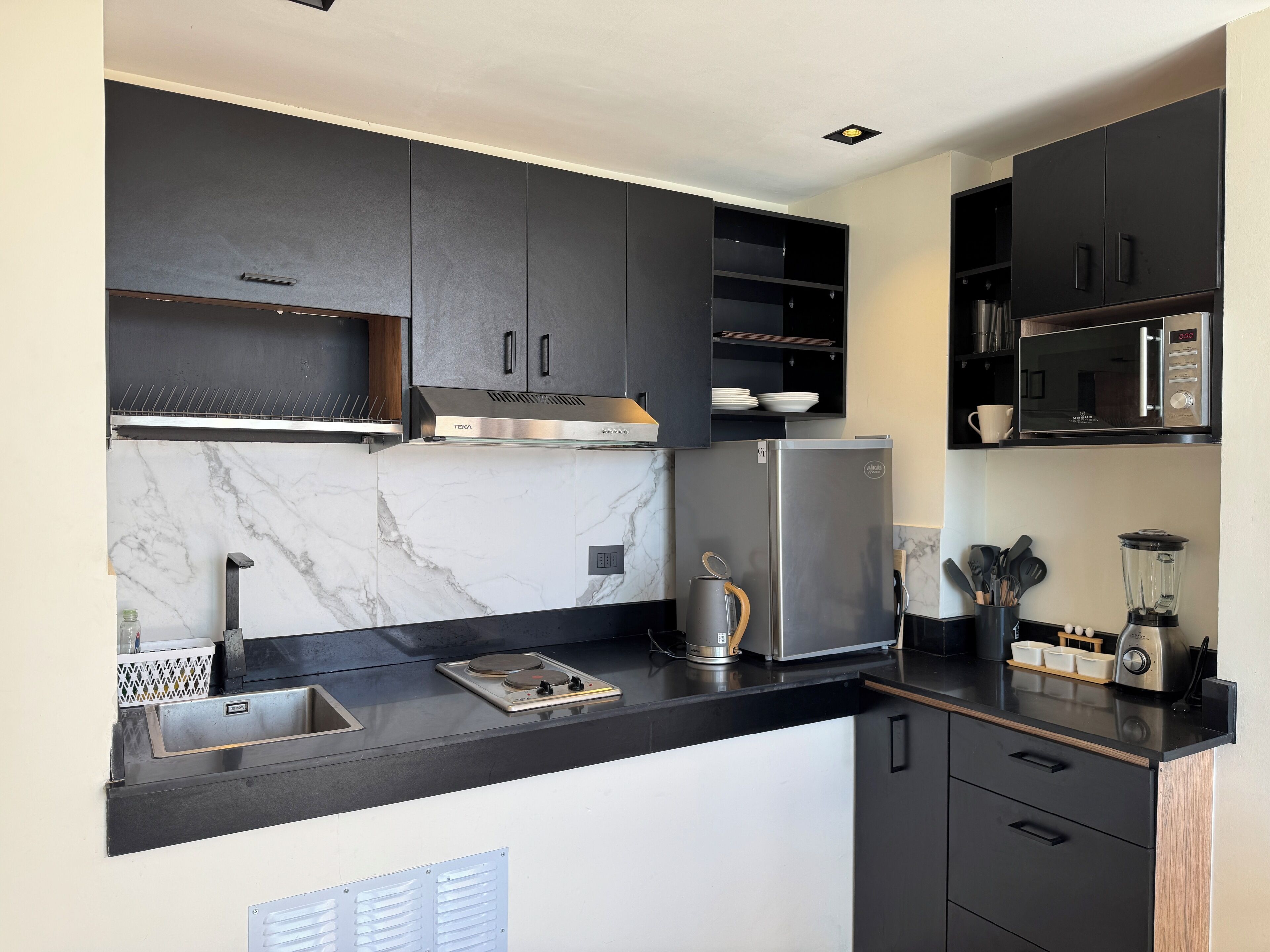 A modern kitchen with dark cabinets, a stainless steel refrigerator, a microwave, and a coffee maker.
