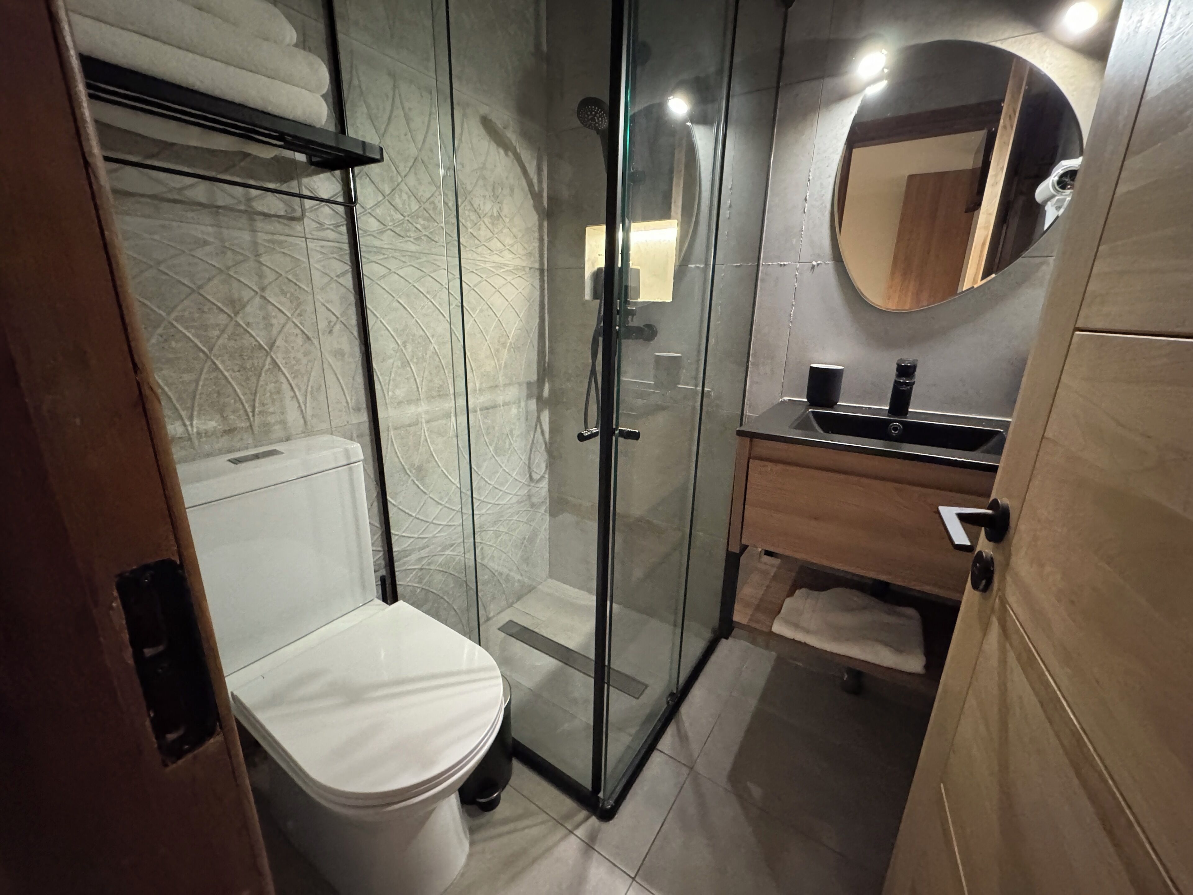 A modern bathroom with a glass shower enclosure, a white toilet, and a wooden vanity with a mirror.