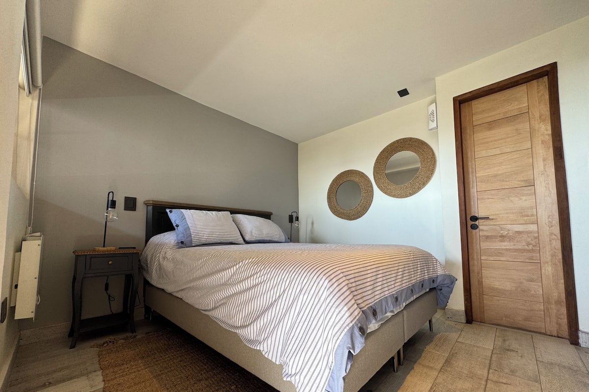Un dormitorio con una cama, una mesita de noche, una puerta de madera y dos espejos en la pared.