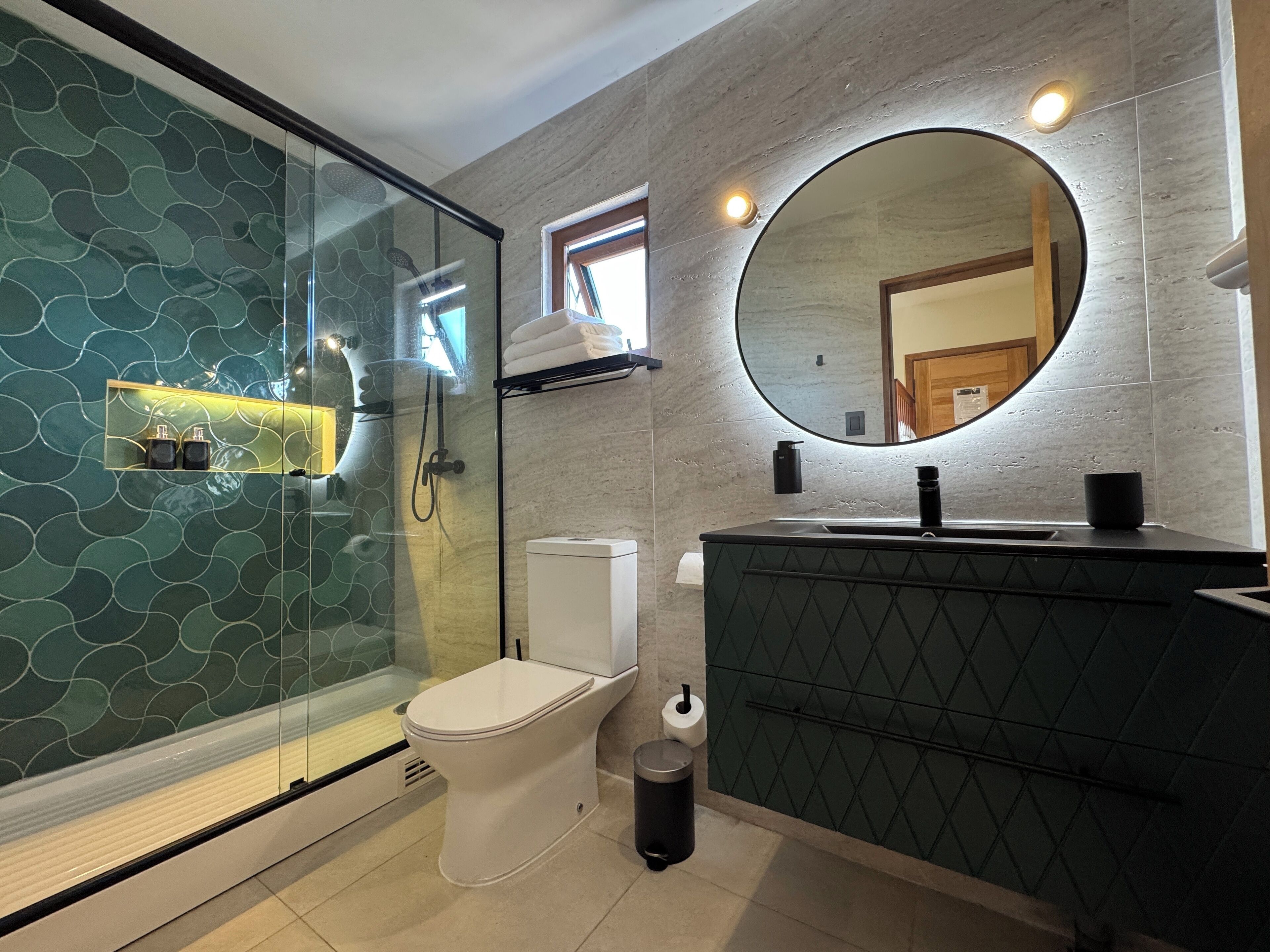 A modern bathroom with a glass-enclosed shower, a toilet, a sink with a mirror, and a towel rack.