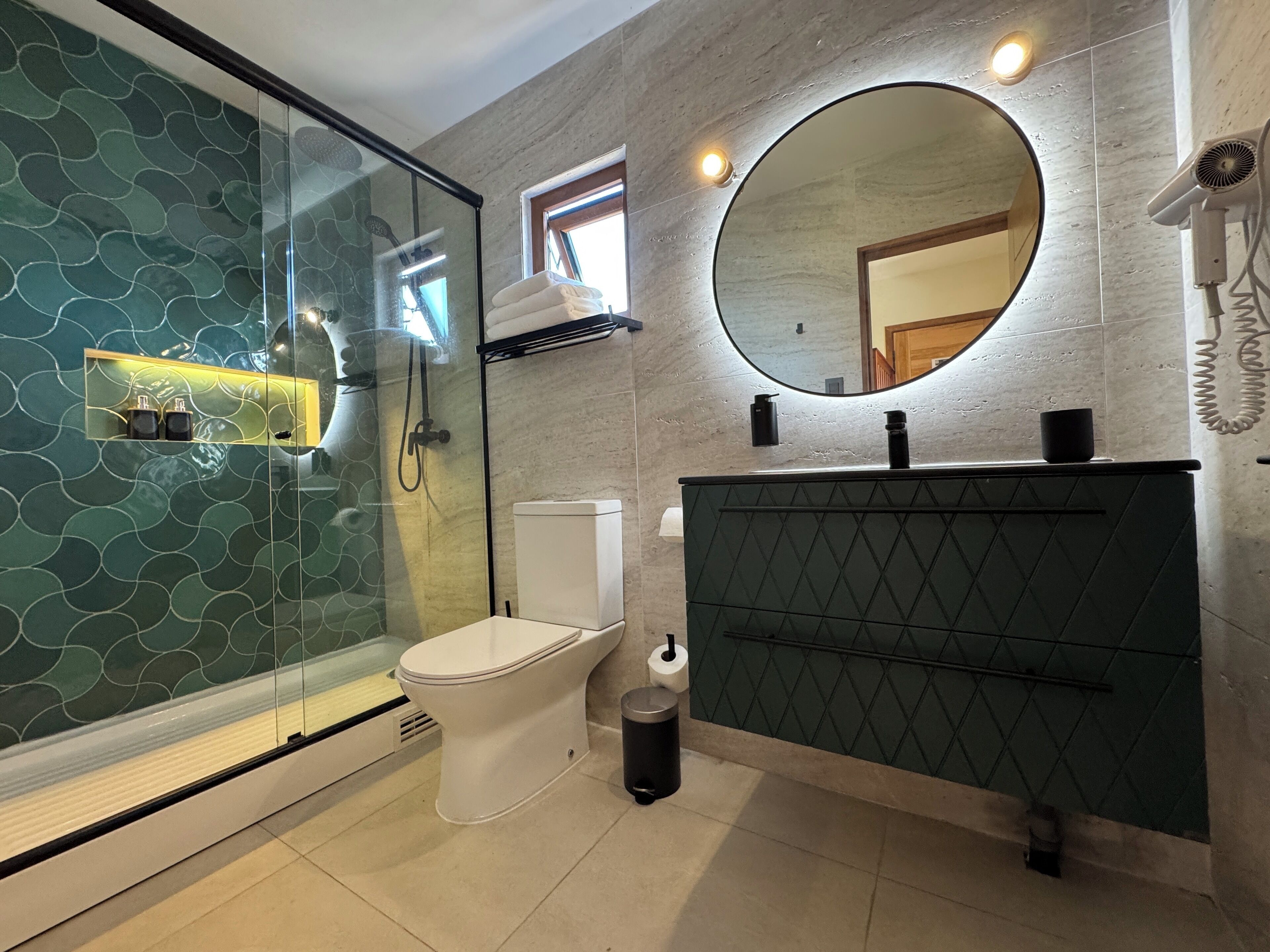 A modern bathroom with a glass shower enclosure, a toilet, a sink with a mirror, and a hairdryer mounted on the wall.