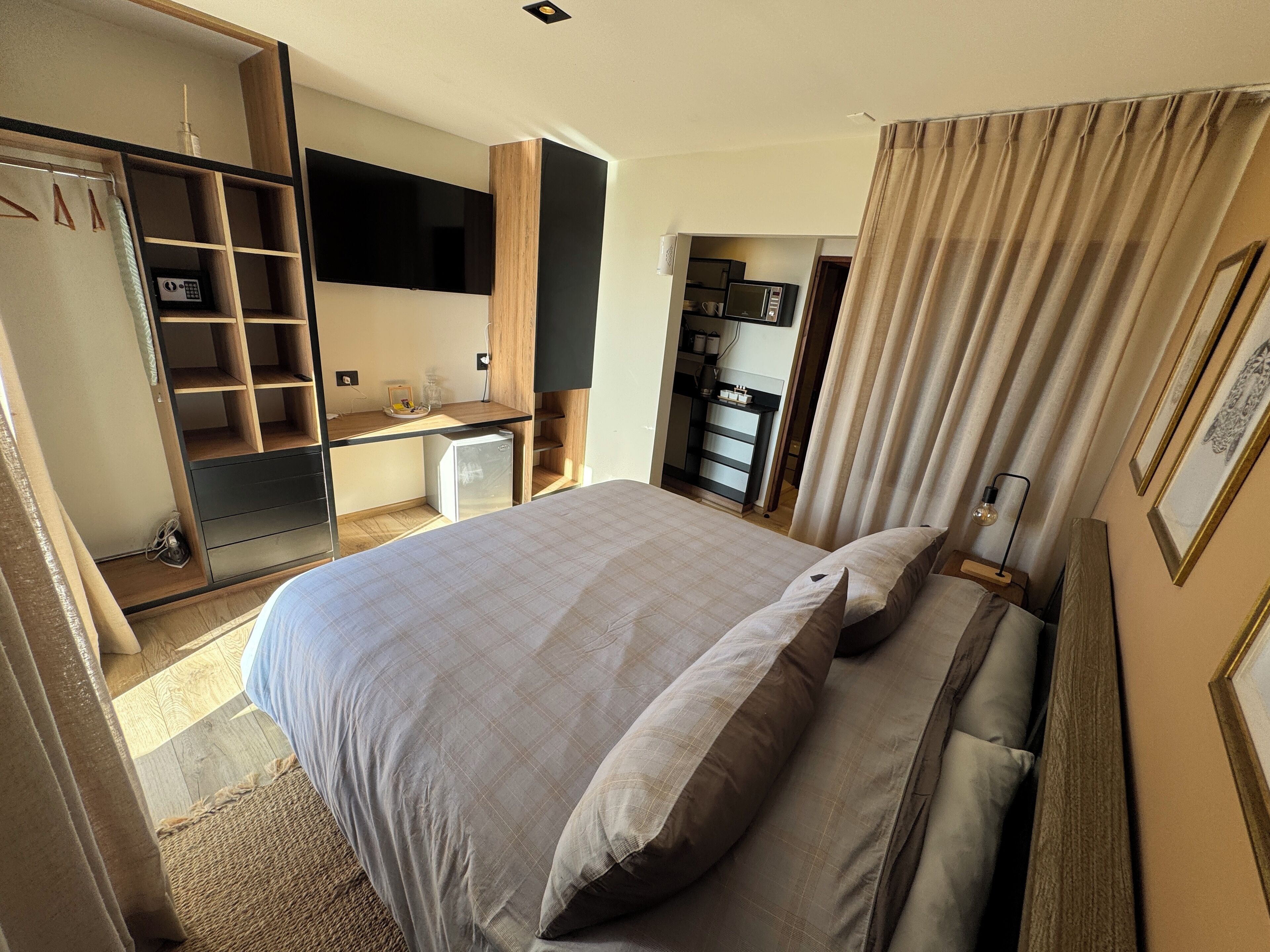 A bedroom with a bed, a desk, a wardrobe, and a kitchenette.