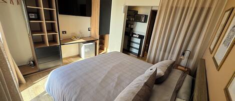 A bedroom with a bed, a desk, a wardrobe, and a kitchenette.