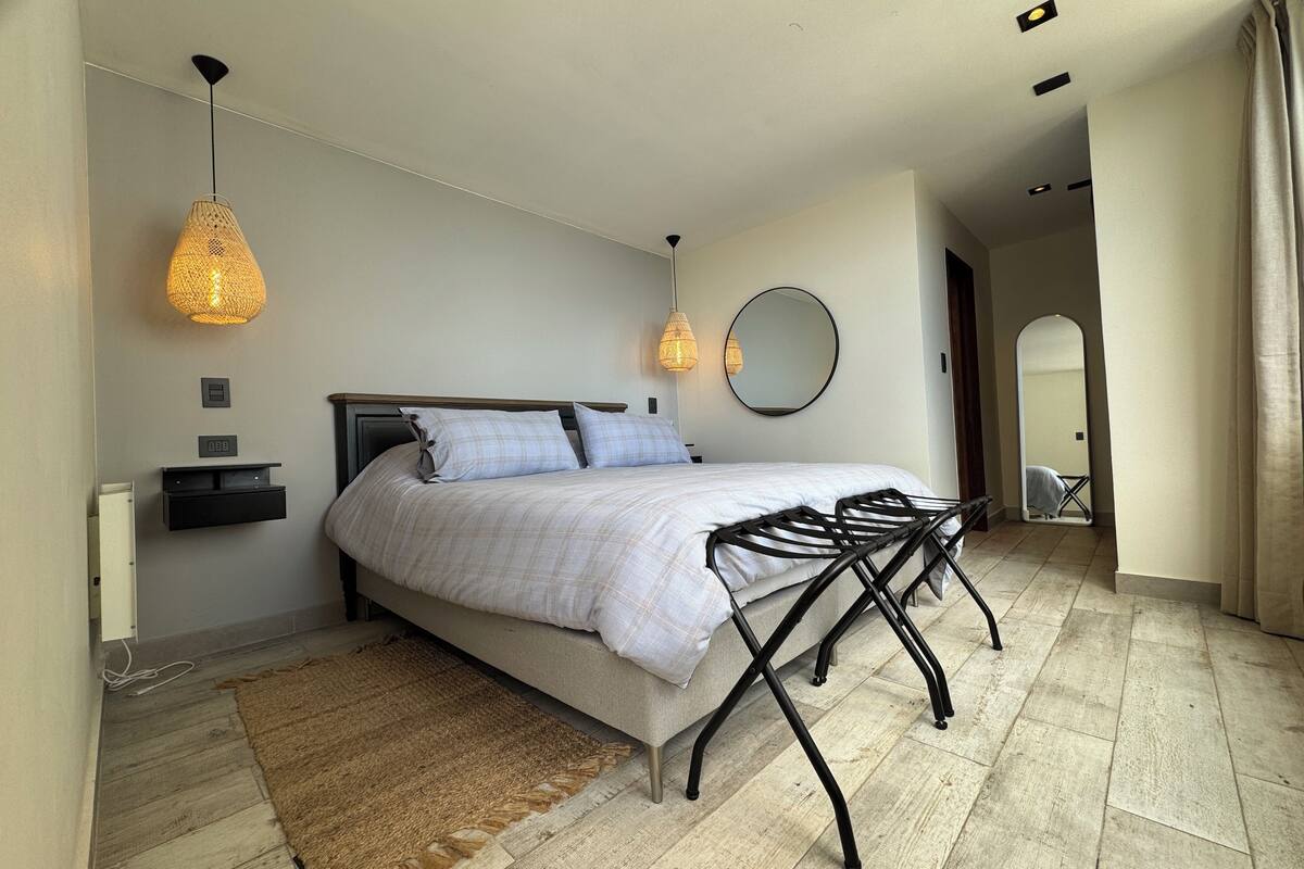 Un dormitorio moderno con cama, mesitas de noche, un espejo y un original banco de metal negro.