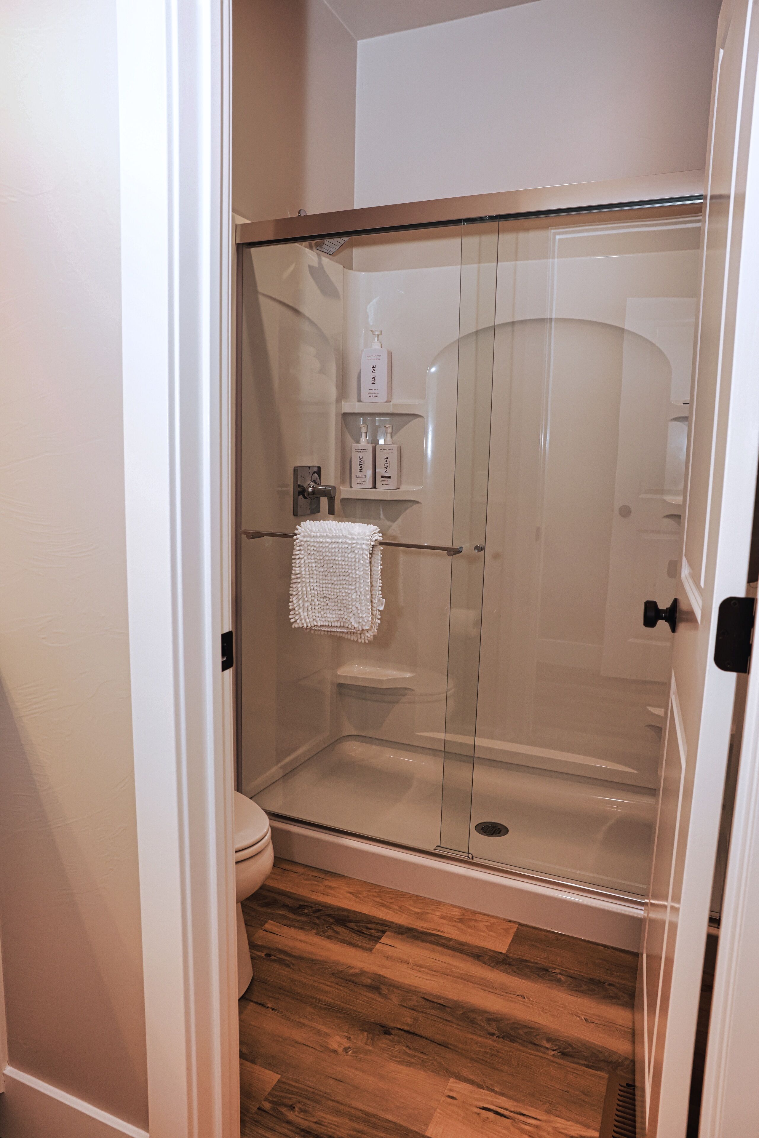 Une cabine de douche fermée par des parois en verre, avec une serviette blanche accrochée à la poignée de la porte.