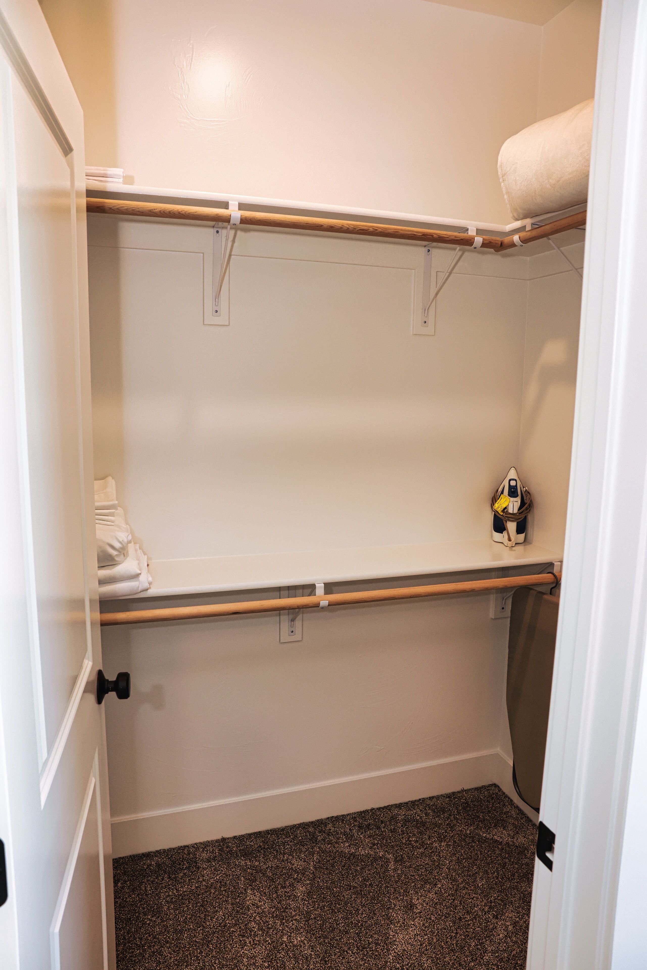 Ein Kleiderschrank mit zwei Holzböden, einer Kleiderstange und einer Tür mit schwarzem Griff.