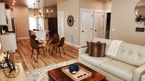 A modern living room with a white sofa, a wooden coffee table, and a dining area with a table and chairs. - NEW! Sparkling 1-Level 2-BDRM King (Billings)