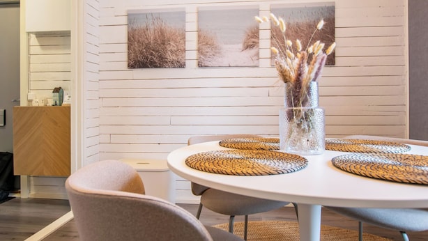 Un comedor con una mesa redonda, sillas y un jarrón con plantas secas.