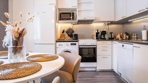 Una cocina moderna con armarios blancos, horno empotrado, microondas y lavavajillas. Hay un comedor con una mesa redonda y sillas.