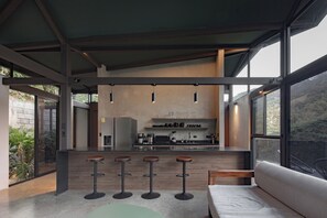 A modern kitchen with a bar area, large windows, and a view of the outdoors. - Elevated Escape - Our jungle house, Minutes away from Playa Mantas, 3BR (Quebrada Ganado)
