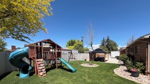 A backyard with a wooden play structure, a slide, and a small garden area.