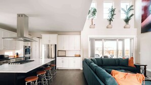 Une cuisine moderne avec des meubles blancs, des appareils en acier inoxydable et un îlot central doté de tabourets.