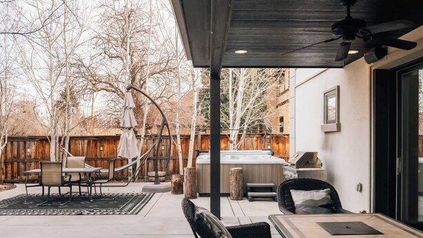 Un patio couvert avec des sièges d’extérieur, un jacuzzi et une clôture en bois en arrière-plan.